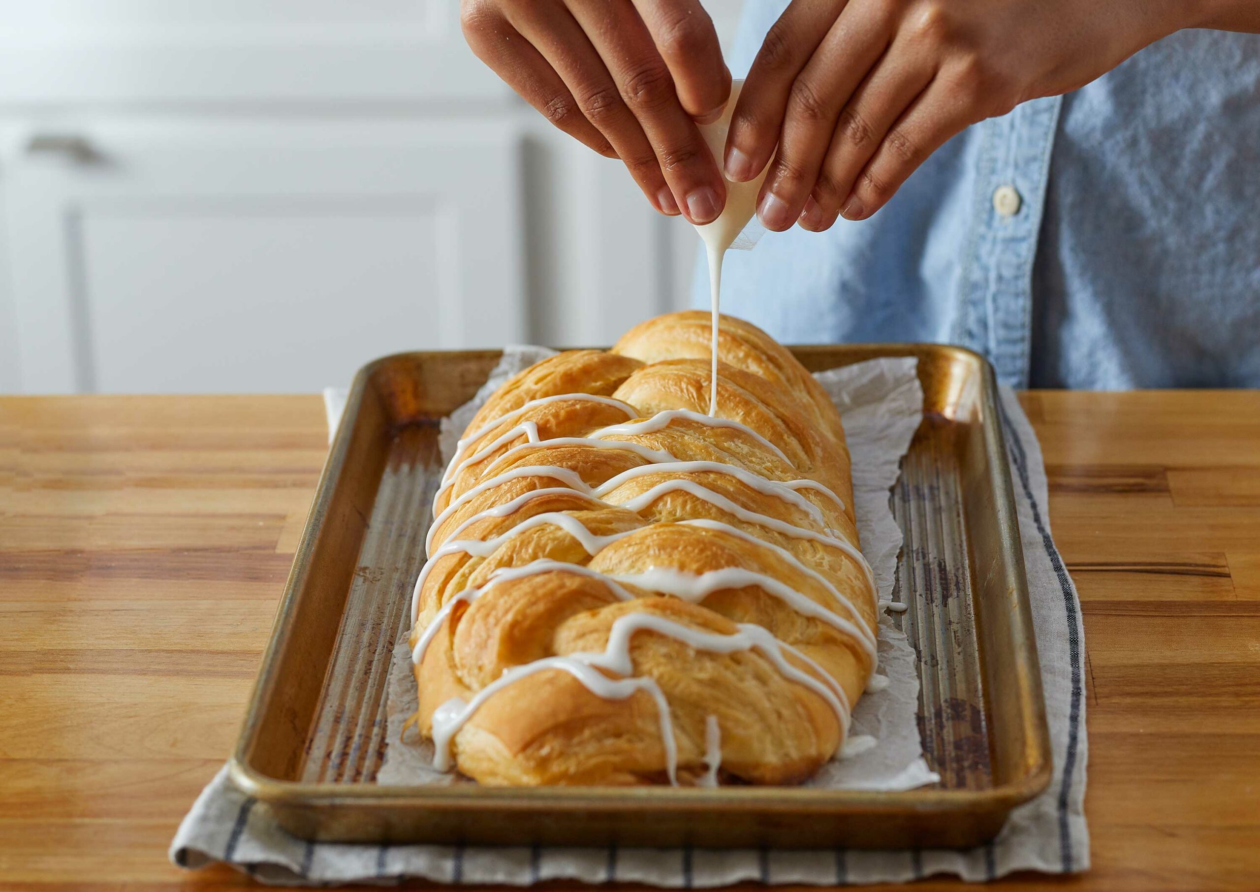 Woman drizzling icing on a cooked Butter Braid Pastry that is sitting on a baking pan.