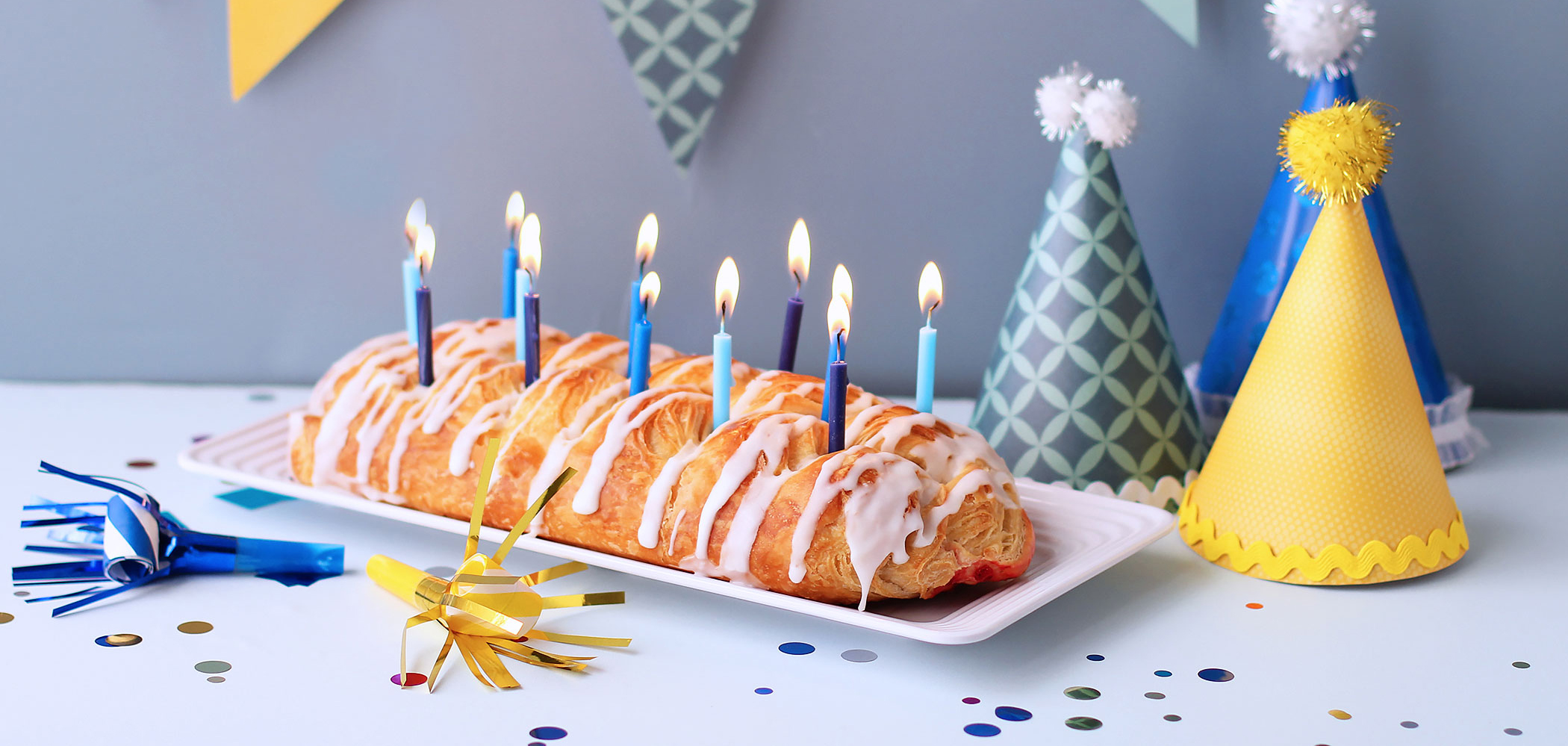 Butter Braid Pastry with candles in it surrounded by birthday hats, confetti, and noise makers.