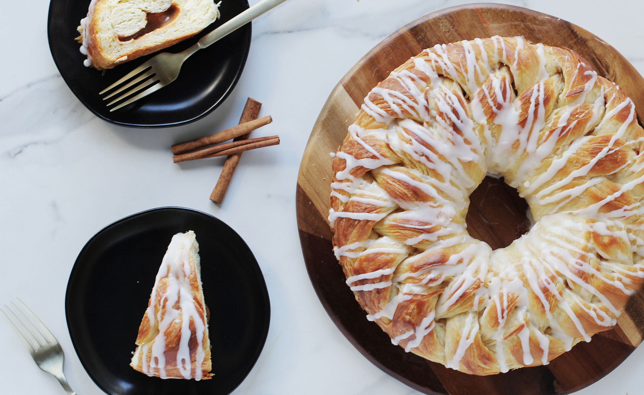 Cinnamon Braided Pastry Ring with two slices of pastries on plates. Cinnamon sticks as garnish.