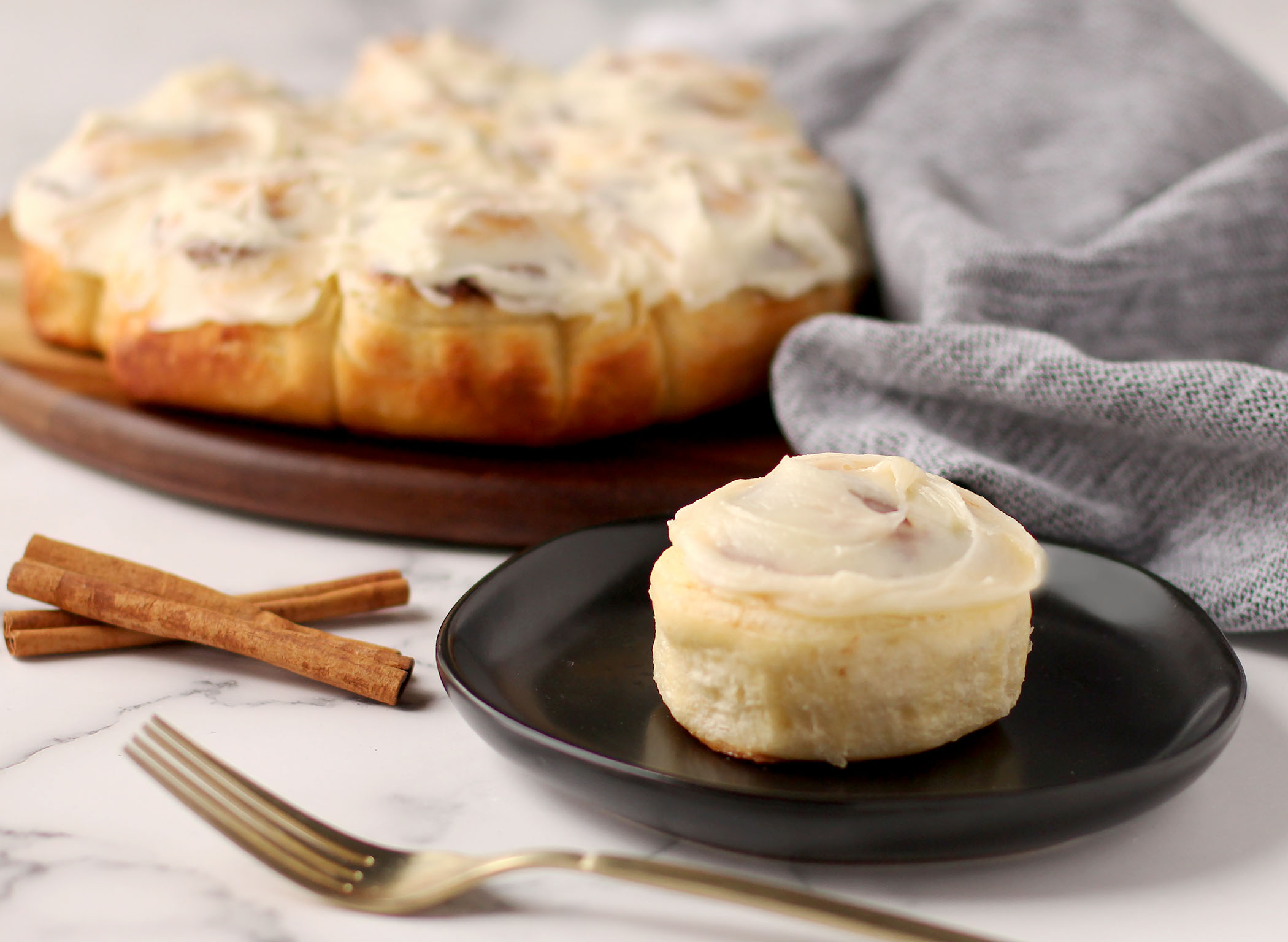 Cinnamon Pastry Rolls together on a serving platter with a single roll on a plate. Cinnamon sticks used as garnish.