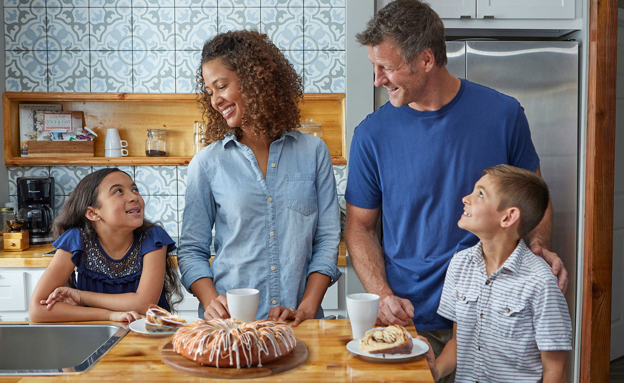 Mom, Dad, daughter, and son in kitchen around the center island. A Cinnamon Braided Pastry Ring is on a tray. Pastry slices are on a few plates.