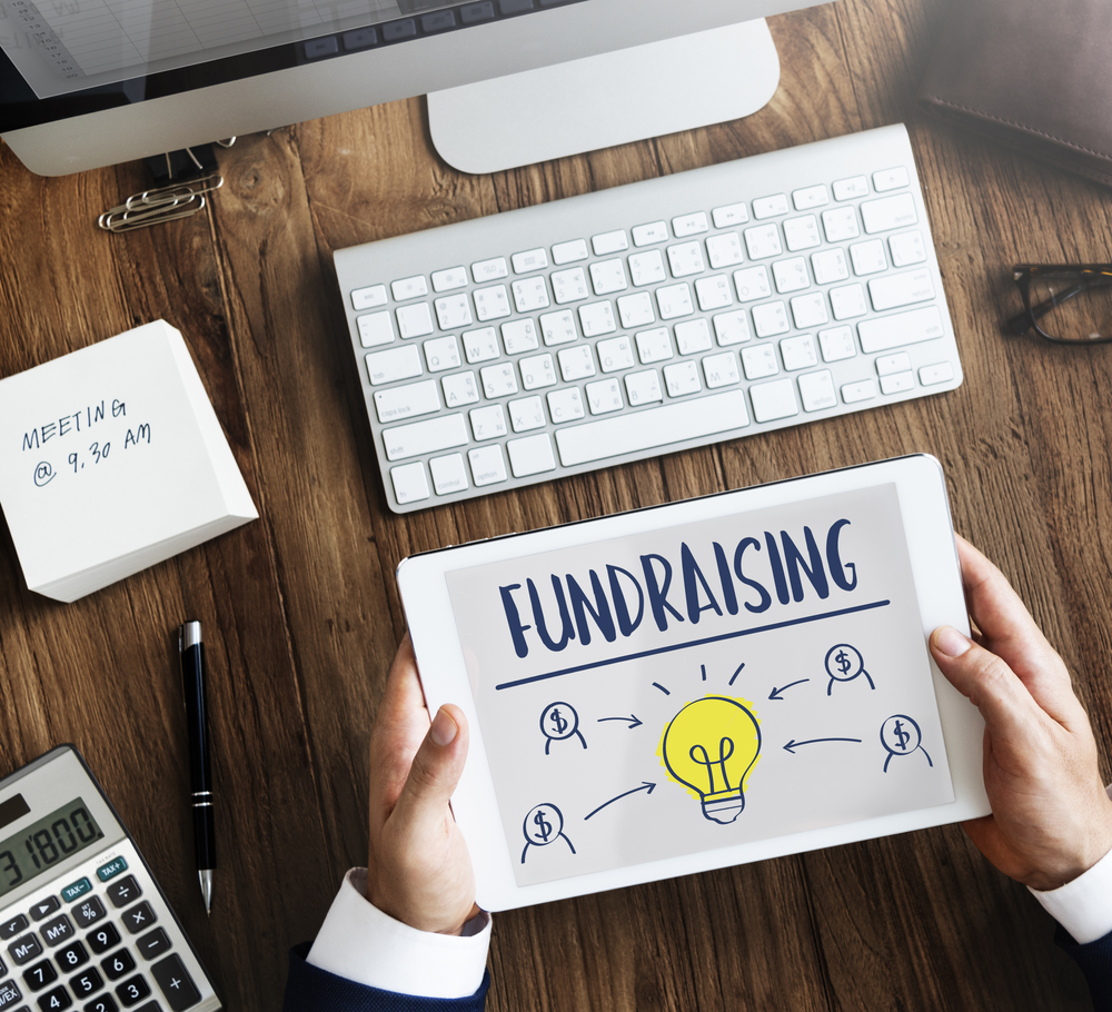 Online Fundraiser - Person's hands holding a tablet with "fundraising" on it at a desk