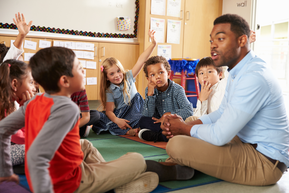 Increase Teacher Involvement - Teacher sitting on floor in circle with kids in a classroom