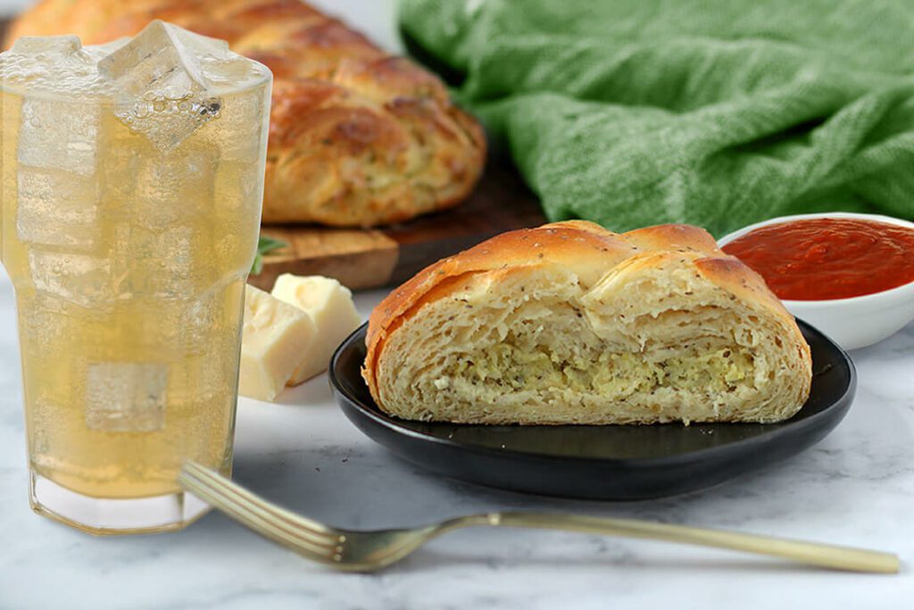 Four Cheese and Herb pastry with slice on a plate. Glass of natural soda next to it.