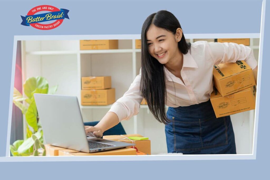 Main Blog Image -Guide to Volunteer Recruitment. Young woman, holding two boxes and typing on a computer. More boxes on shelves behind her.