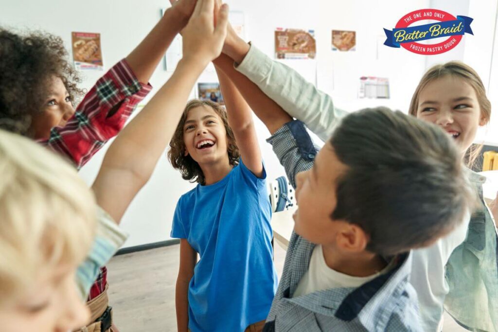 Secrets to Successful Fundraising #1 - Stay Motivated and Optimistic - group of middle school students high-fiving. Butter Braid Pastry fundraising materials are on the wall behind them.