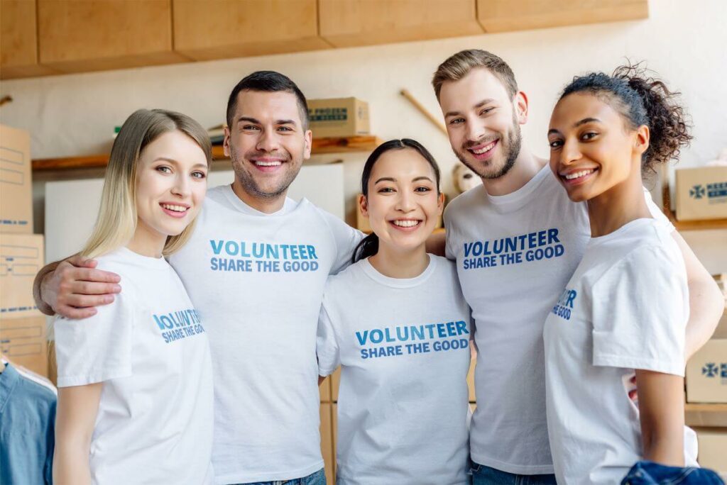 Volunteer retention blog image - Group of five volunteers, men and women, wearing shirts that say "Volunteer - Share the Good". There are boxes of pastries in the background.