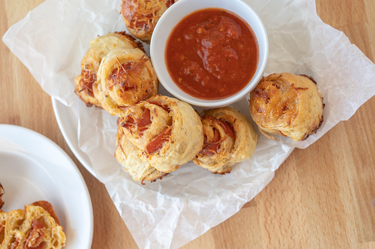 A plate full of Four Cheese Pepperoni Pinwheels with a bowl of marinara sauce in the center.