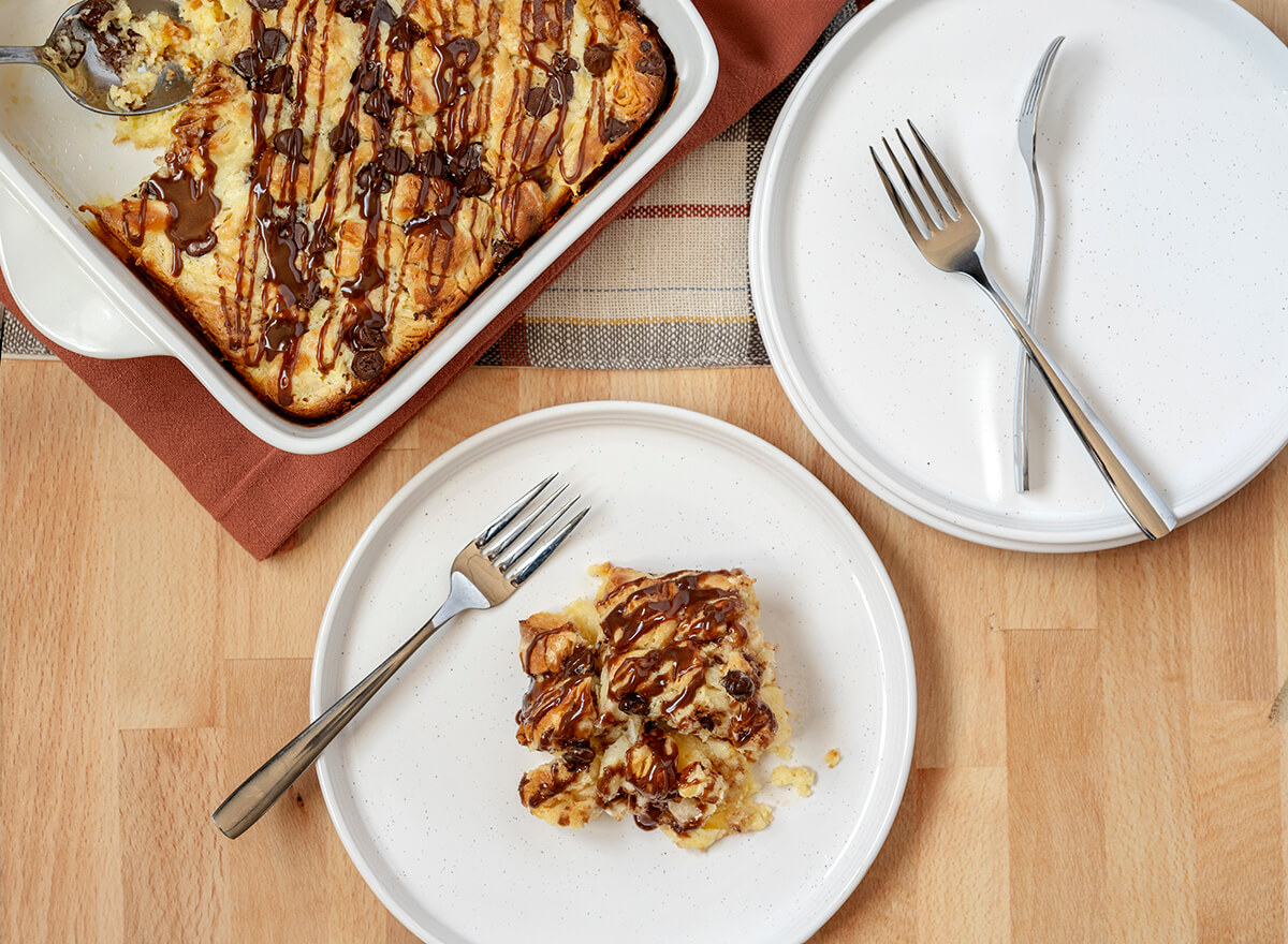 Bavarian Crème Breakfast Bake - the bake is in a pan and next to a stack of plates and silverware. One plate has a serving of the breakfast bake on it.