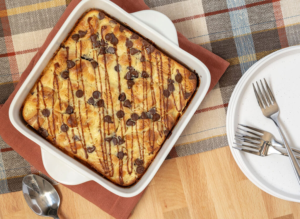 Bavarian Crème Breakfast Bake in a pan next to a plate and silverware. A plaid table runner is underneath the pan.