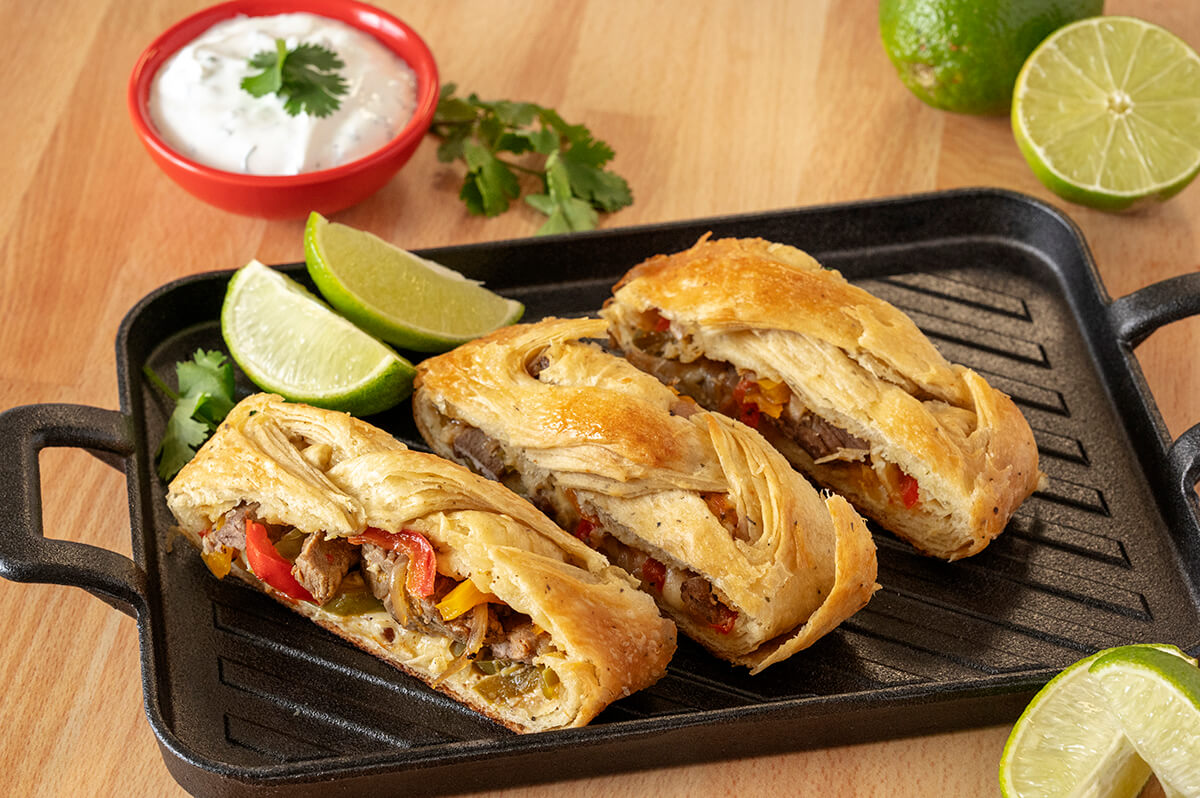 Three slices of Fajita Pastry on a cast iron serving tray next to several slices of limes. There is also a bowl of cilantro lime crème.