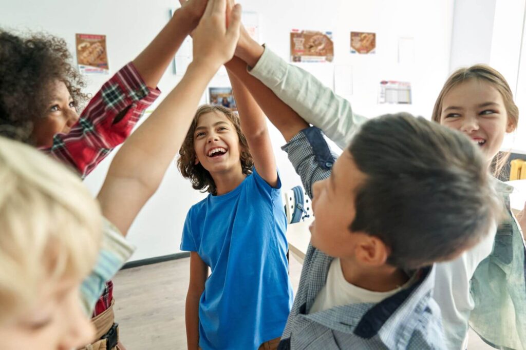 Ways to Motivate Your Sellers - group of middle school students high-fiving. Butter Braid Pastry fundraising materials are on the wall behind them.