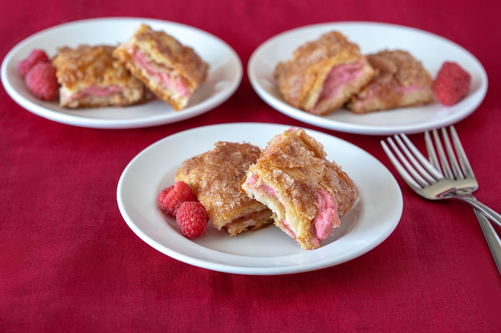 Three plates with two servings of Raspberry Sopapilla Cheesecake on each plate. Each plate also has red raspberries used as garnish.