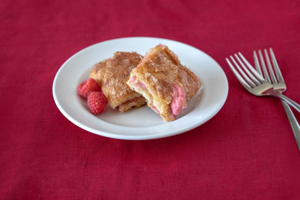 A plate with two servings of Raspberry Sopapilla Cheesecake alongside red raspberries used for garnish.