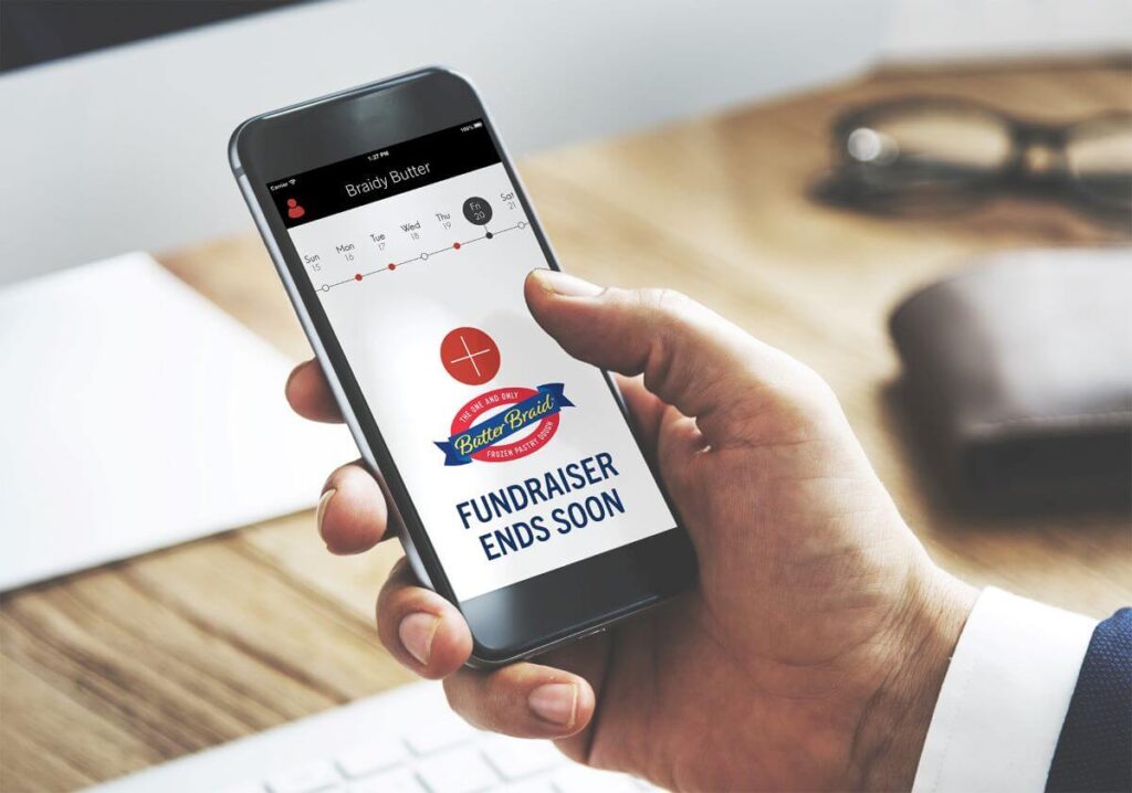 A person holding a cell phone. On the phone screen is a reminder featuring the Butter Braid® Pastry logo and "Fundraiser Ends Soon"