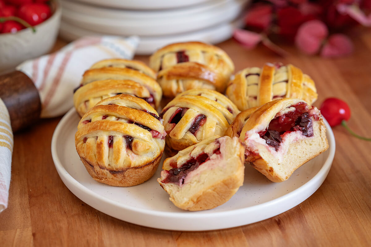 Several Mini Cherry Pies on a serving dish. One is cut in half showing the filling inside.