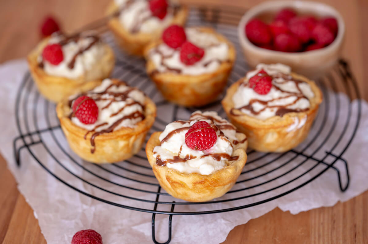 Bavarian Cream Tartlets on a wire rack next to a bowl of raspberries.